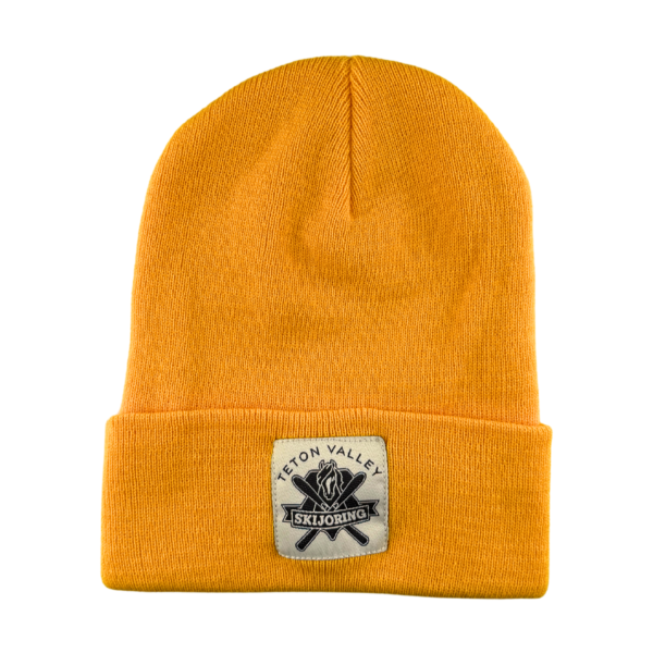 Yellow knit fold-up beanie with a square white patch on the front showing the black & white Teton Valley Skijoring logo